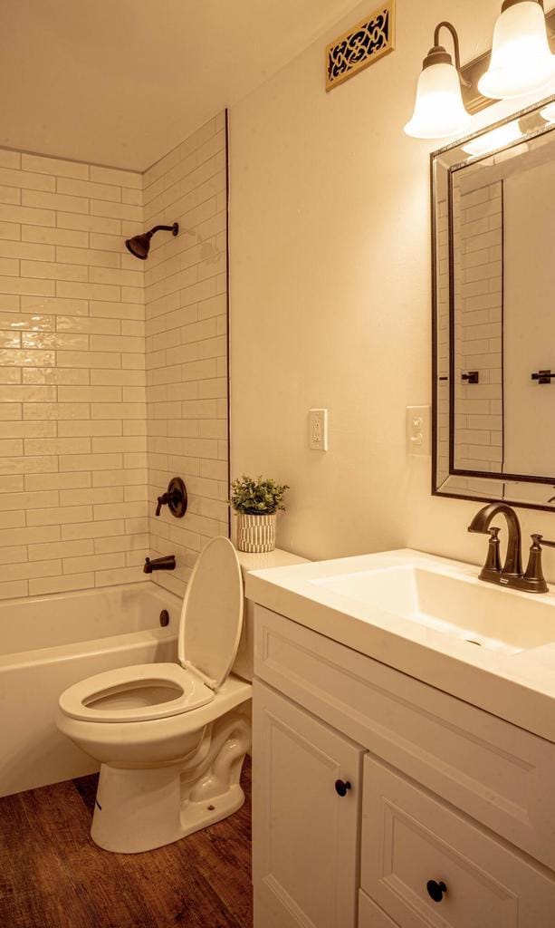 full bathroom with tiled shower / bath combo, vanity, hardwood / wood-style floors, and toilet