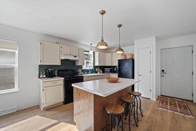 kitchen with sink, black appliances, a center island, light hardwood / wood-style flooring, and backsplash