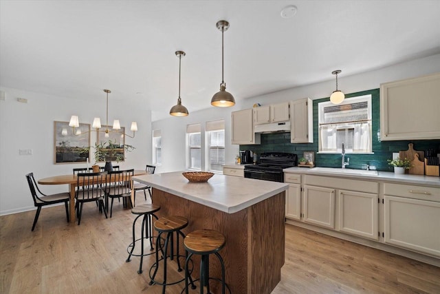 kitchen featuring sink, black electric range, hanging light fixtures, and a kitchen island