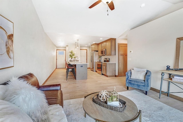 living room featuring ceiling fan, lofted ceiling, sink, and light hardwood / wood-style floors