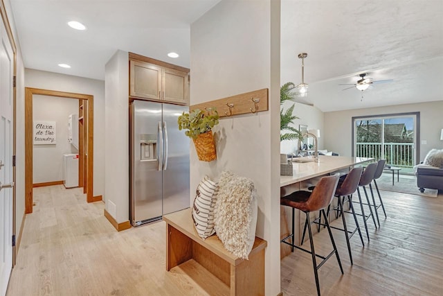 kitchen with ceiling fan, a kitchen breakfast bar, stainless steel refrigerator with ice dispenser, decorative light fixtures, and light wood-type flooring