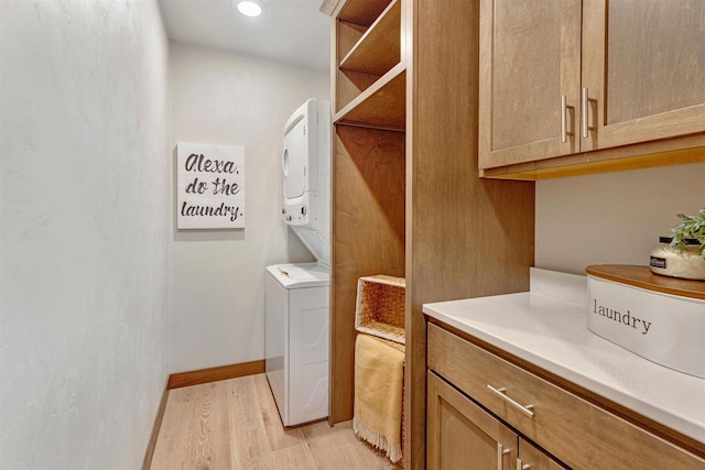 clothes washing area with stacked washer / drying machine, cabinets, and light wood-type flooring