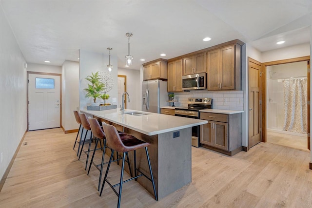 kitchen with sink, a breakfast bar area, decorative light fixtures, light wood-type flooring, and stainless steel appliances