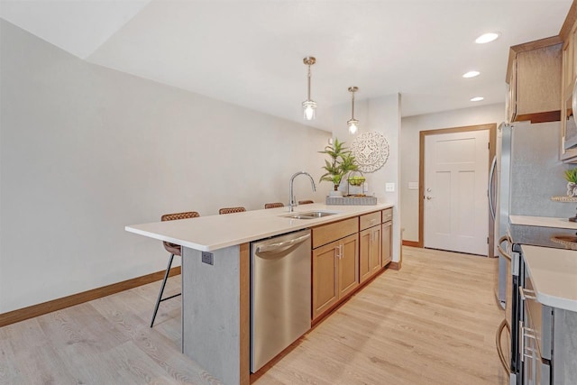 kitchen featuring sink, light hardwood / wood-style flooring, appliances with stainless steel finishes, a kitchen bar, and decorative light fixtures