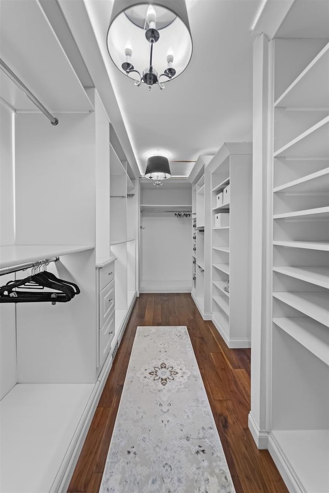 spacious closet with dark wood-type flooring and a chandelier