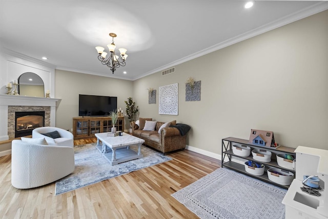 living room with an inviting chandelier, hardwood / wood-style floors, crown molding, and a stone fireplace