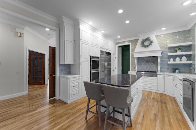 kitchen with a breakfast bar area, white cabinets, a center island, stainless steel appliances, and custom range hood