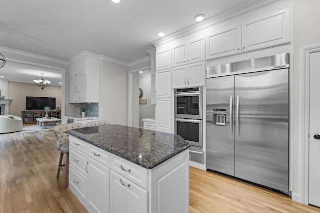 kitchen with white cabinetry, appliances with stainless steel finishes, crown molding, and dark stone counters