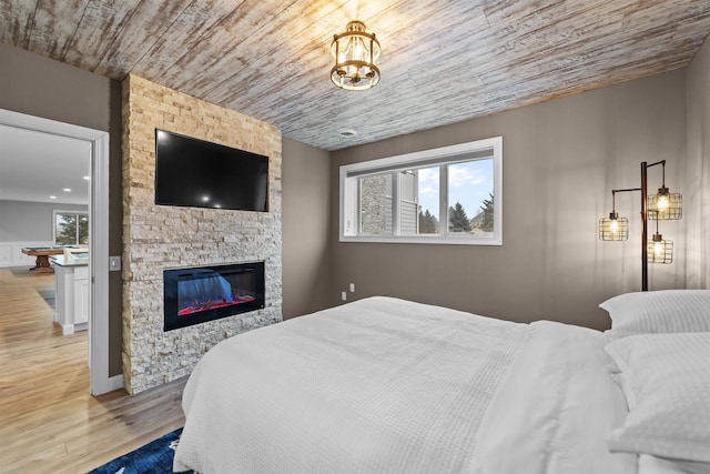 bedroom featuring wooden ceiling, a stone fireplace, and light wood-type flooring