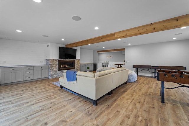 living room featuring a stone fireplace, beam ceiling, and light wood-type flooring