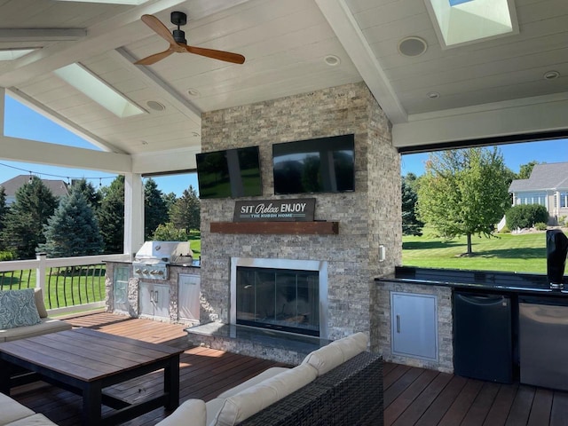 deck with area for grilling, ceiling fan, an outdoor stone fireplace, and an outdoor kitchen