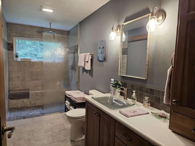 bathroom featuring tiled shower, vanity, decorative backsplash, tile patterned floors, and toilet