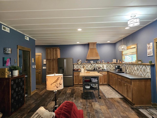 kitchen featuring stainless steel refrigerator with ice dispenser, sink, hanging light fixtures, kitchen peninsula, and custom range hood