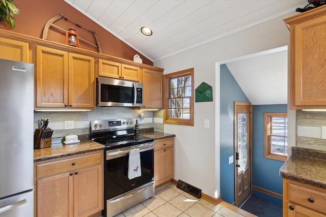 kitchen featuring backsplash, stainless steel appliances, light tile patterned flooring, vaulted ceiling, and dark stone counters