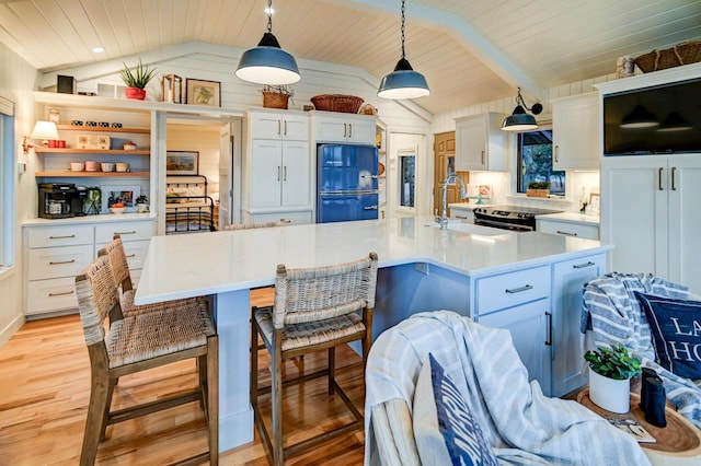 kitchen with sink, vaulted ceiling with beams, decorative light fixtures, refrigerator, and a center island with sink