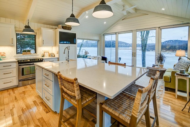 kitchen featuring hanging light fixtures, electric range, white cabinets, and a center island with sink