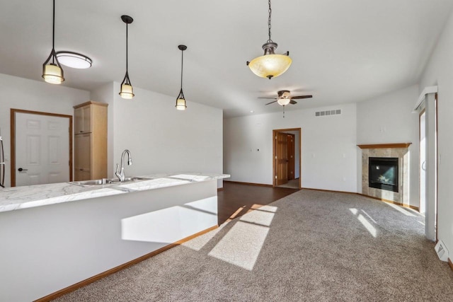 kitchen featuring a tile fireplace, decorative light fixtures, sink, dark colored carpet, and ceiling fan