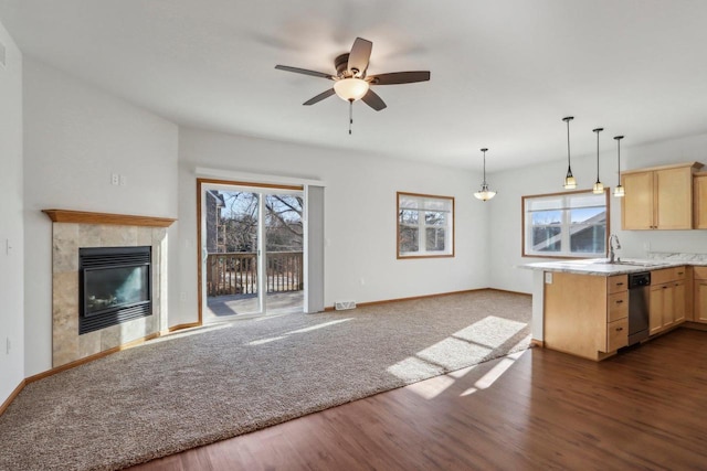 kitchen with light brown cabinetry, hanging light fixtures, dark hardwood / wood-style floors, dishwasher, and a tile fireplace