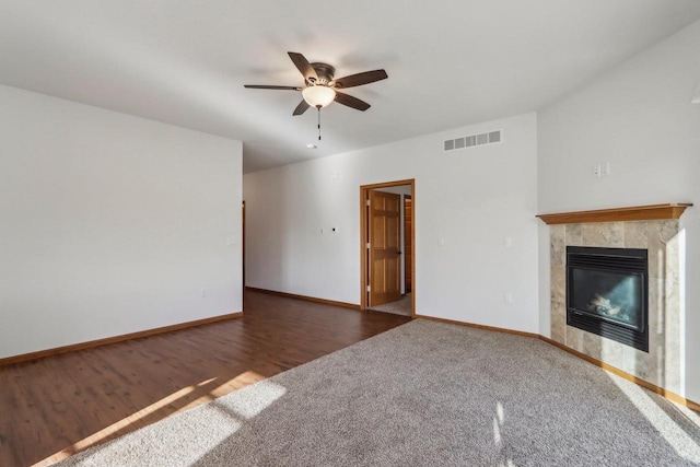 unfurnished living room with a tile fireplace, dark wood-type flooring, and ceiling fan