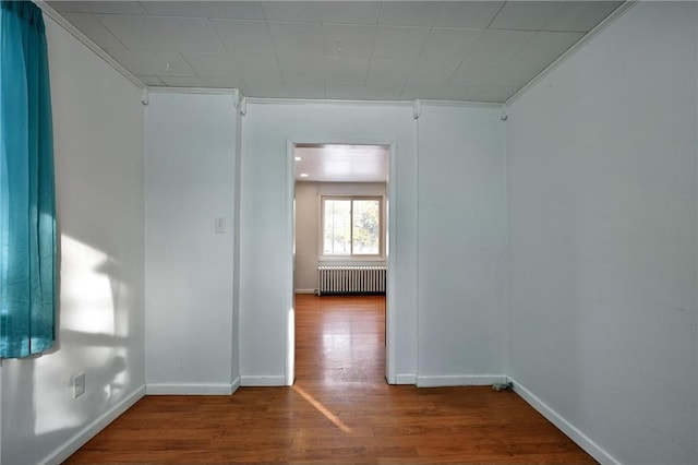 empty room with ornamental molding, wood-type flooring, and radiator