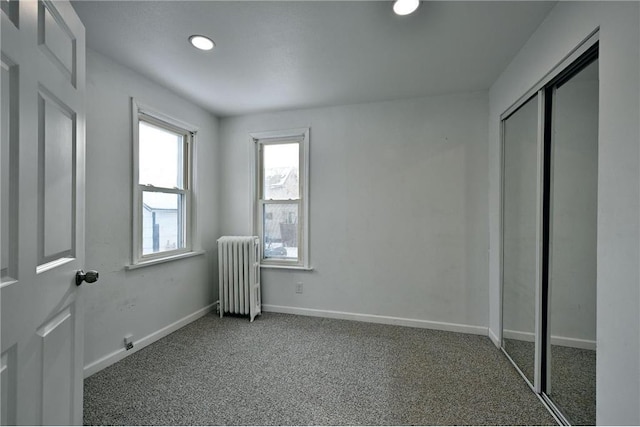 unfurnished bedroom featuring radiator, a closet, and dark colored carpet