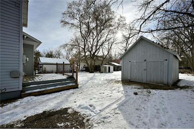 yard layered in snow featuring a storage shed and a wooden deck