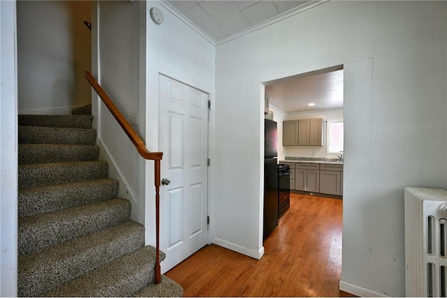 staircase with crown molding, radiator, sink, and hardwood / wood-style flooring