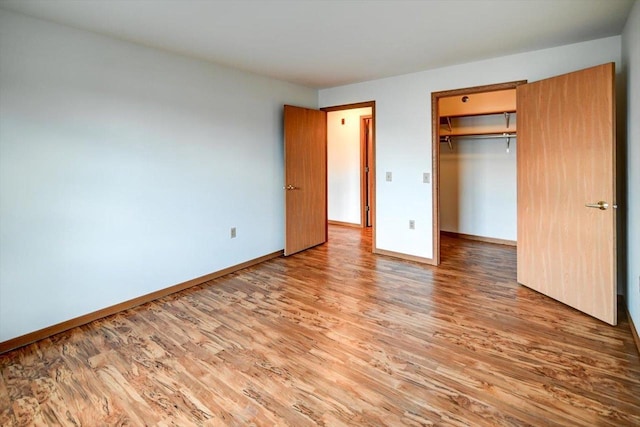 unfurnished bedroom featuring a spacious closet, wood-type flooring, and a closet