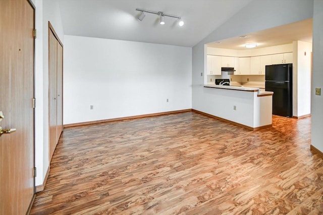 kitchen featuring black refrigerator, hardwood / wood-style floors, white cabinets, vaulted ceiling, and kitchen peninsula