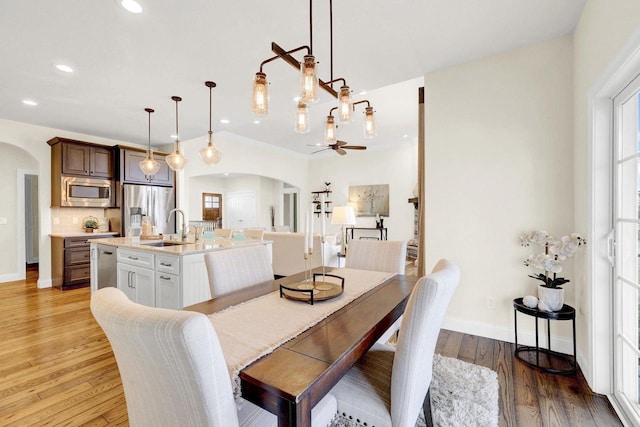 dining room with sink, ceiling fan with notable chandelier, and light hardwood / wood-style flooring