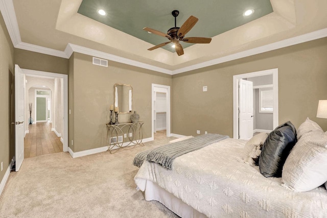 bedroom featuring ornamental molding, a walk in closet, ceiling fan, a tray ceiling, and light carpet