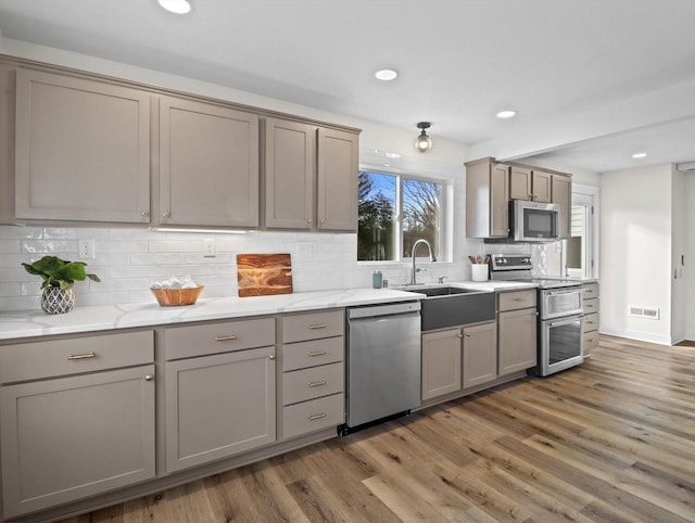 kitchen featuring sink, gray cabinetry, wood-type flooring, appliances with stainless steel finishes, and light stone countertops