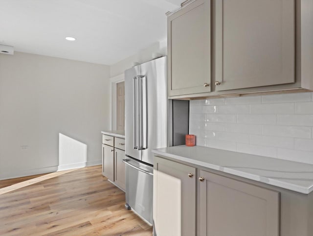 kitchen with high end fridge, gray cabinetry, light stone counters, light hardwood / wood-style flooring, and decorative backsplash