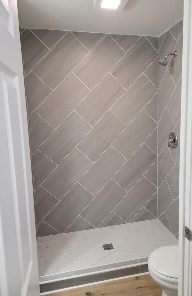 bathroom featuring wood-type flooring, toilet, and a tile shower