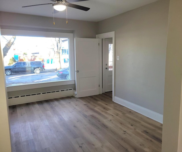 unfurnished room with wood-type flooring, ceiling fan, and baseboard heating