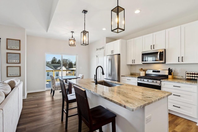 kitchen with pendant lighting, stainless steel appliances, light stone counters, and a center island with sink