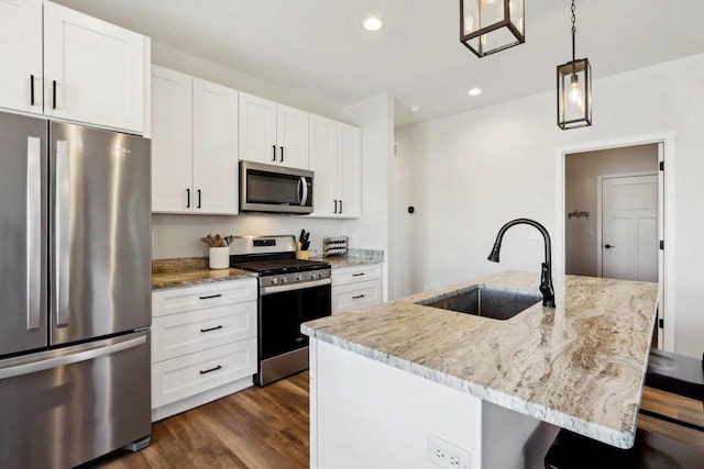 kitchen featuring sink, hanging light fixtures, stainless steel appliances, light stone countertops, and a kitchen island with sink