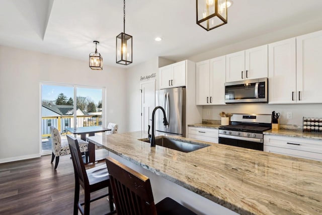 kitchen featuring a kitchen bar, sink, white cabinetry, hanging light fixtures, and stainless steel appliances