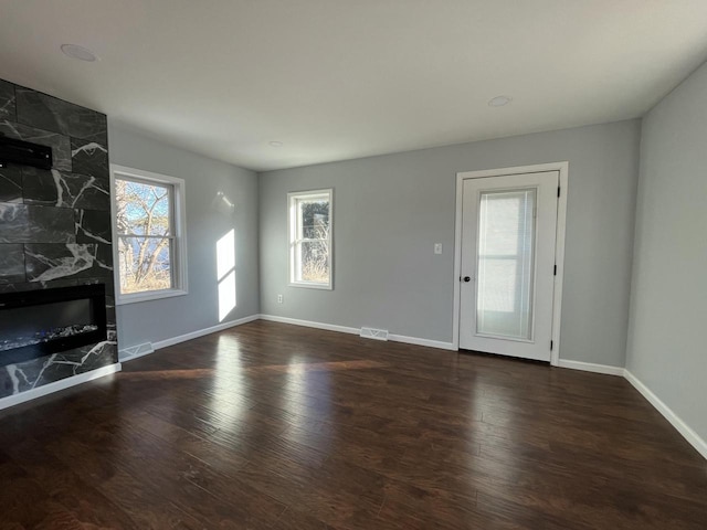 unfurnished living room with a healthy amount of sunlight, dark wood-type flooring, and a fireplace