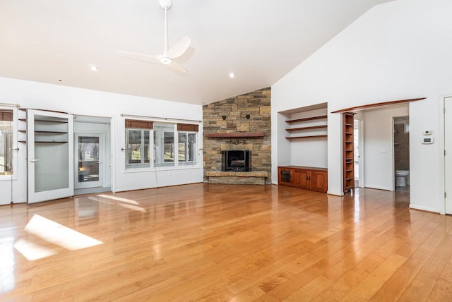 unfurnished living room with ceiling fan, a stone fireplace, high vaulted ceiling, and light hardwood / wood-style flooring