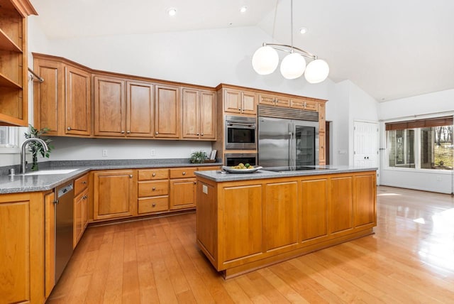 kitchen with sink, appliances with stainless steel finishes, a center island, decorative light fixtures, and light wood-type flooring