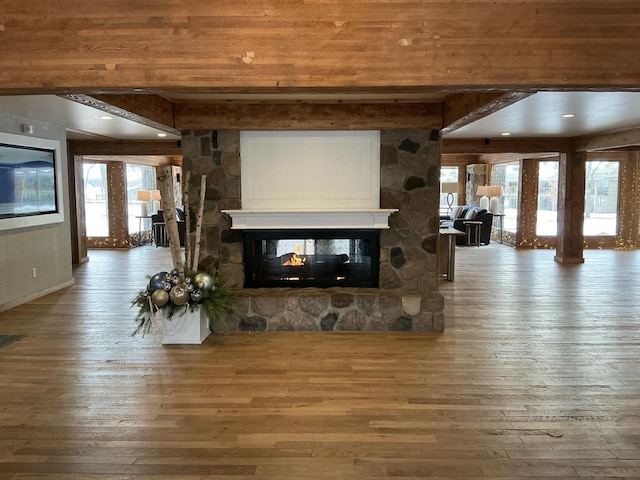 unfurnished living room featuring hardwood / wood-style floors, a stone fireplace, plenty of natural light, and beamed ceiling