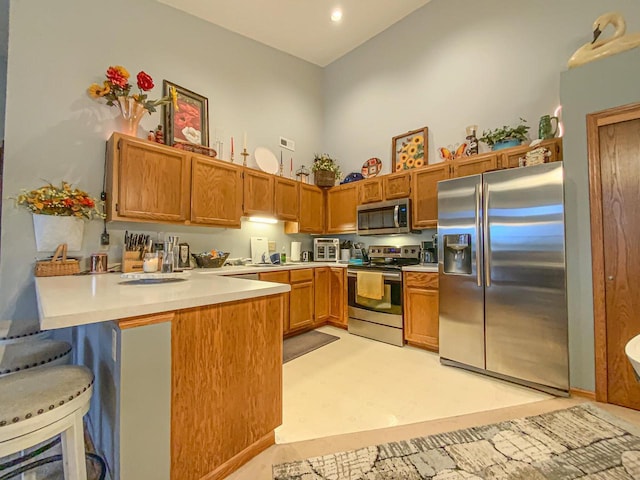 kitchen with a breakfast bar, appliances with stainless steel finishes, kitchen peninsula, and a high ceiling