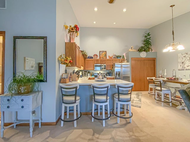 kitchen featuring pendant lighting, high vaulted ceiling, a chandelier, kitchen peninsula, and stainless steel appliances