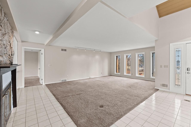 unfurnished living room featuring rail lighting, light colored carpet, and beam ceiling