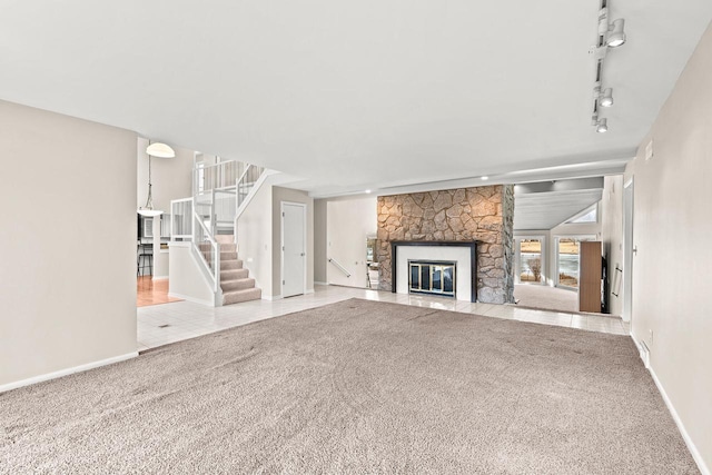 unfurnished living room featuring a stone fireplace, light carpet, and rail lighting