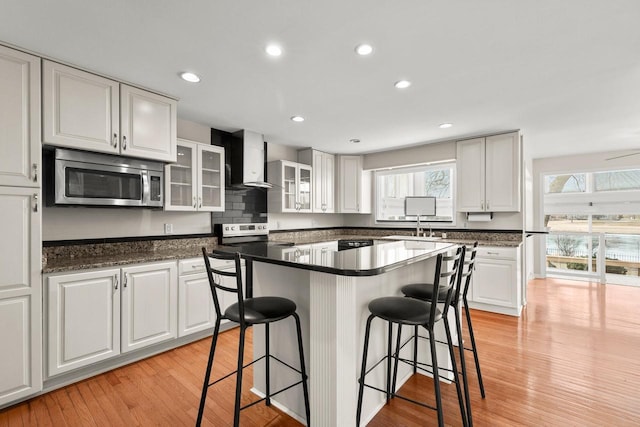 kitchen featuring white cabinetry, stainless steel appliances, and wall chimney range hood