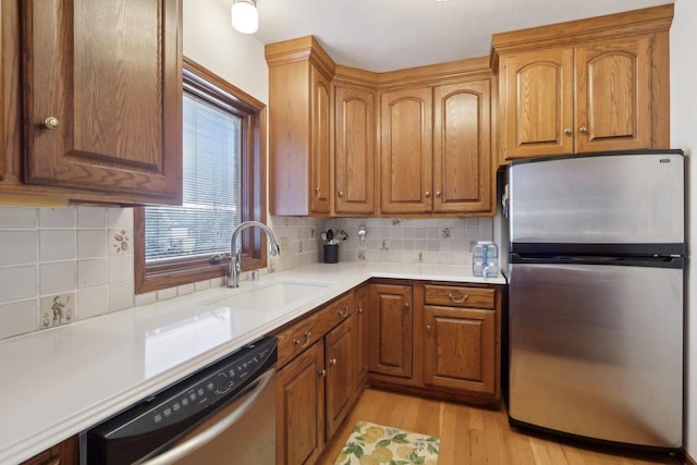 kitchen with brown cabinets, a sink, stainless steel appliances, light wood-style floors, and light countertops