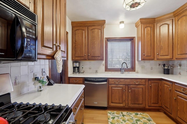 kitchen with range with gas cooktop, black microwave, dishwasher, light wood-style flooring, and a sink