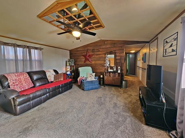 carpeted living room with lofted ceiling, wooden walls, and ceiling fan